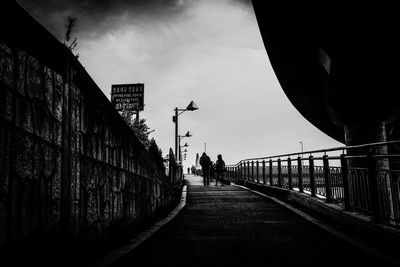 Silhouette people walking on footpath against sky