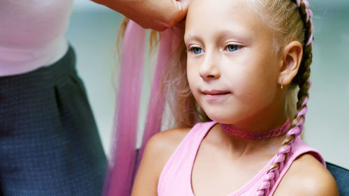 Beautiful blond girl, of seven years old, braided two pigtails, do a hairstyle with pink locks of