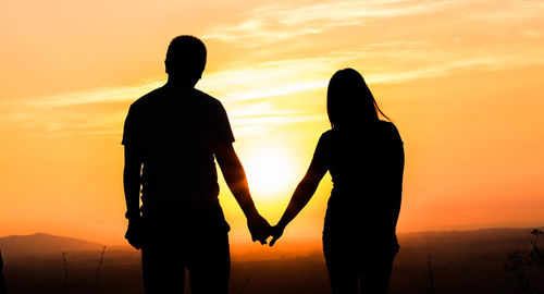 Silhouette couple standing against orange sky during sunset