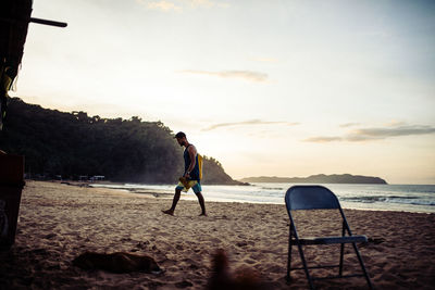 Man standing on beach against sky during sunset