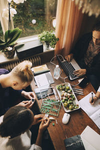 High angle view of friends working on project while teenager studying at table in house