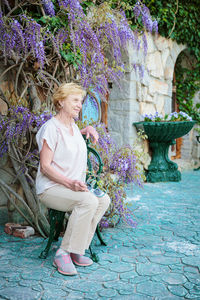 Elderly woman posing on a bench near a blooming branch of wisteria