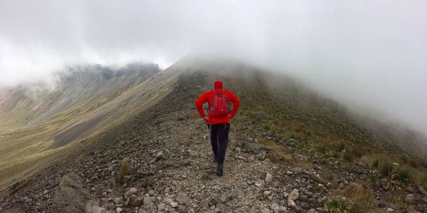 Rear view of man walking on mountain against clouds