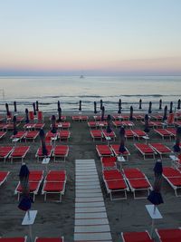 Empty lounge chairs at beach against clear sky during sunset