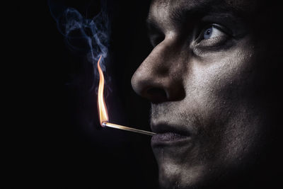 Close-up portrait of man smoking cigarette against black background