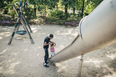 Father holding hands of daughter walking on slide at playground