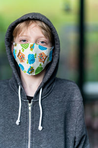 Young person wearing hood and face covering looking at camera