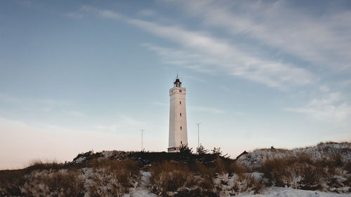 Lighthouse on field by building against sky