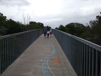 People walking on footbridge against sky