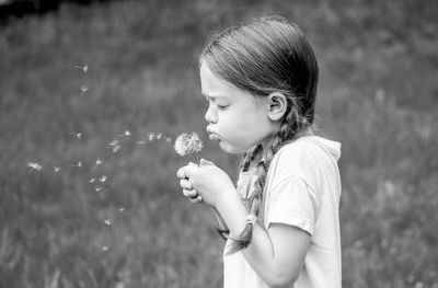 Side view of girl blowing on dandelion seeds