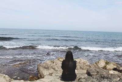 Rear view of woman sitting on beach against clear sky