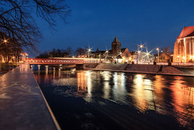 Illuminated bridge over river by buildings against sky at night