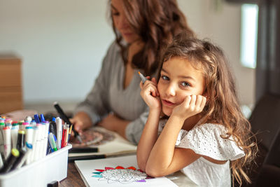 Portrait of cute girl sitting by mother at home