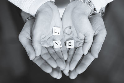 Cropped hands of couple holding love text with wedding ring