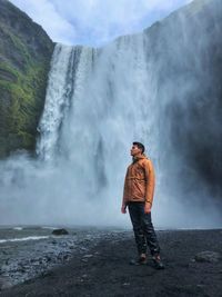 Full length of man standing by waterfall on mountains