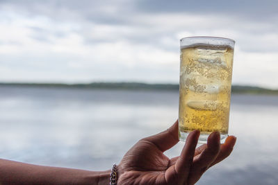Hand holding glass of water against sky
