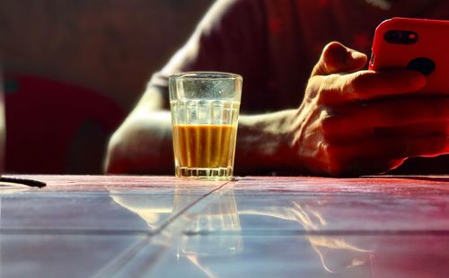 Close-up of human hand using mobile phone by tea on table