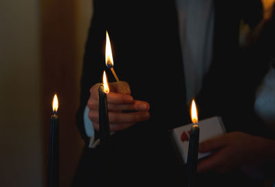 Midsection of person lighting candles with matchstick in darkroom