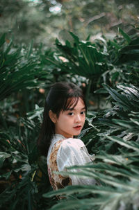 Portrait of young woman standing amidst plants