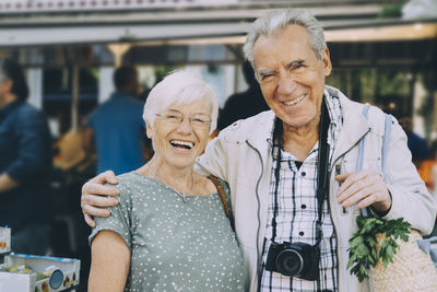 Portrait of smiling senior couple with arm around standing at market in city