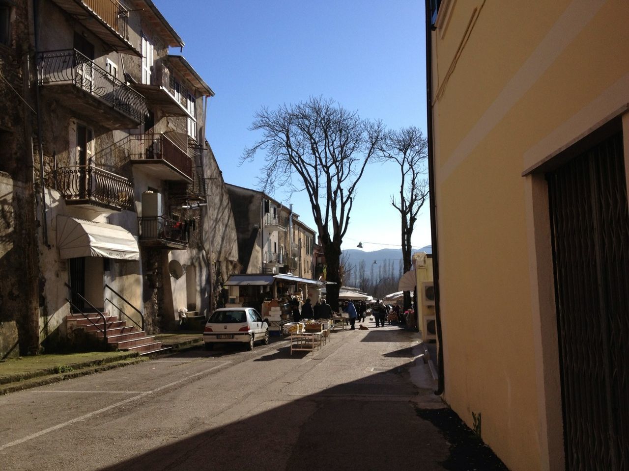 architecture, building exterior, built structure, the way forward, clear sky, street, city, diminishing perspective, narrow, alley, building, residential structure, sunlight, shadow, residential building, tree, vanishing point, road, transportation, day