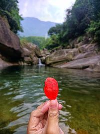 Close-up of hand holding leaf against waterfall