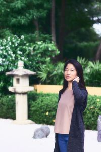 Portrait of young woman standing against trees