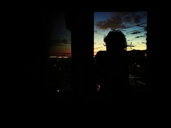 Silhouette man looking through window at sunset