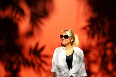 Young woman wearing sunglasses standing against wall on sunny day