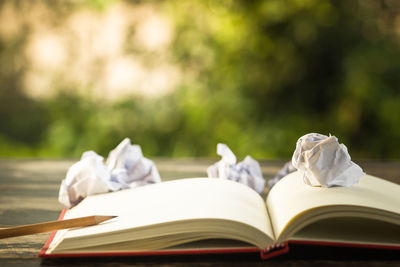 Close-up of open book with pencil and crumpled papers on table