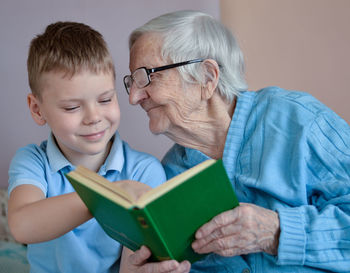 Portrait of white-hair eldery woman 90 years old with her grandson at home, reading book together