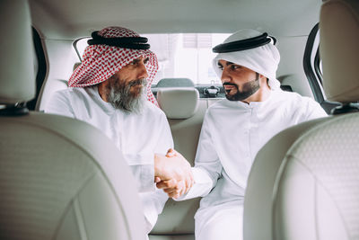 Men wearing dish dash shaking hands while sitting in car