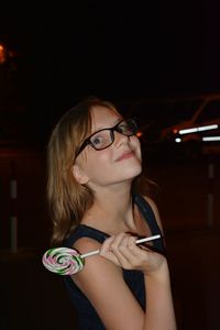 Smiling girl wearing eyeglasses holding lollipop at night