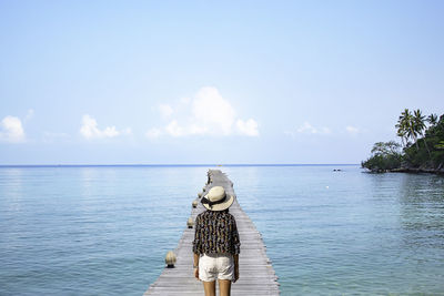 Rear view of woman standing on pier over sea against blue sky