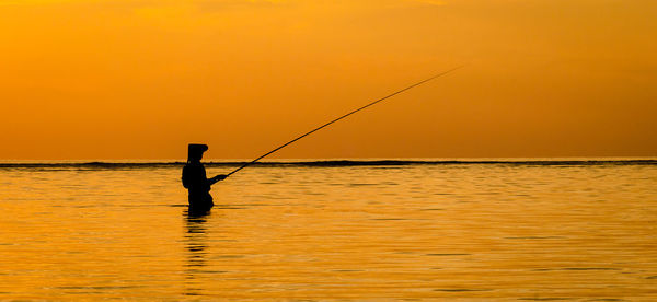 Silhouette fisherman fishing in sea against clear sky during sunset