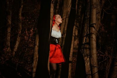 Portrait of young woman standing by tree trunk in forest