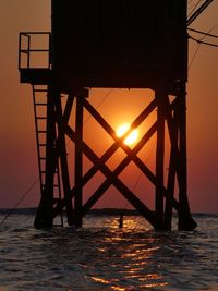 Silhouette bridge over sea against sky during sunset