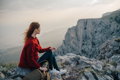 Young woman sitting on rock against mountain