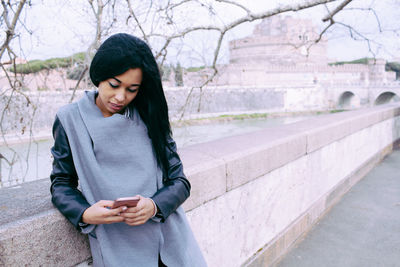 Young woman using mobile phone while standing on tree