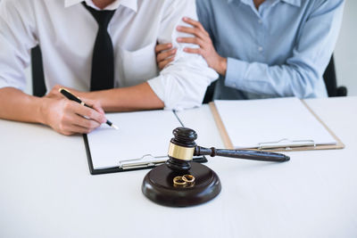 Midsection of man and woman signing divorce papers while sitting on table at courtroom