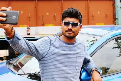 Young man taking selfie while leaning on car