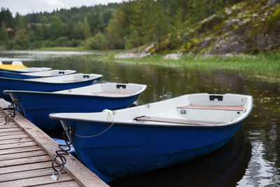 Blue empty boats on the lake along the wooden pier closeup cloudy autumn sky and forest background