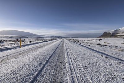 Tire tracks on snow covered road against sky