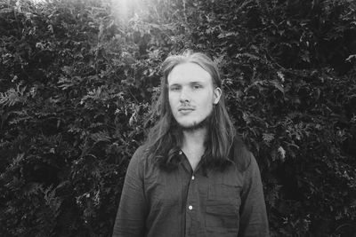 Portrait of young man standing against trees