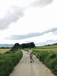 Man cycling on road amidst field against sky