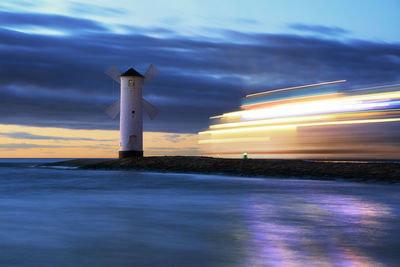 Lighthouse by sea against sky at night
