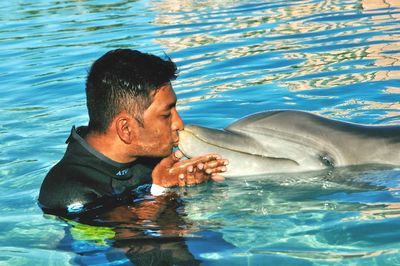 Young man kissing dolphin while swimming in pool