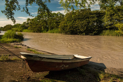 Abandoned boat on riverbank against sky