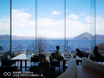 People sitting in restaurant by sea against sky