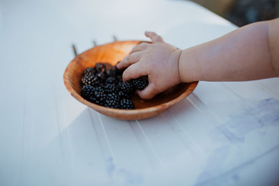 Cropped hand of baby picking blackberries from plate at table